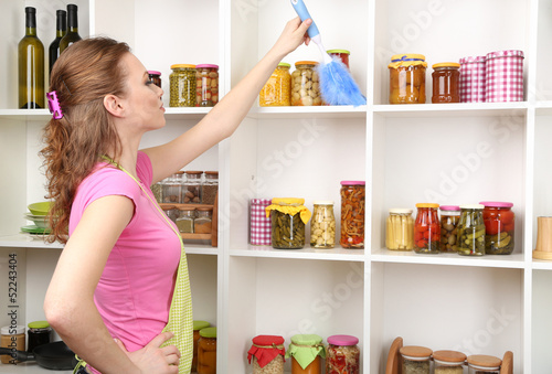 Young housewife cleaning up kitchen on grey background