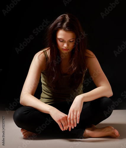 A young woman sitting on the floor, isolated on black background © shefkate