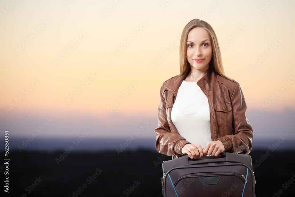 Woman with a suitcase on the sea beach  at sunset