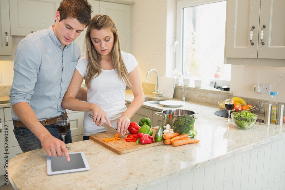 Woman cutting vegetables with man using tablet computer
