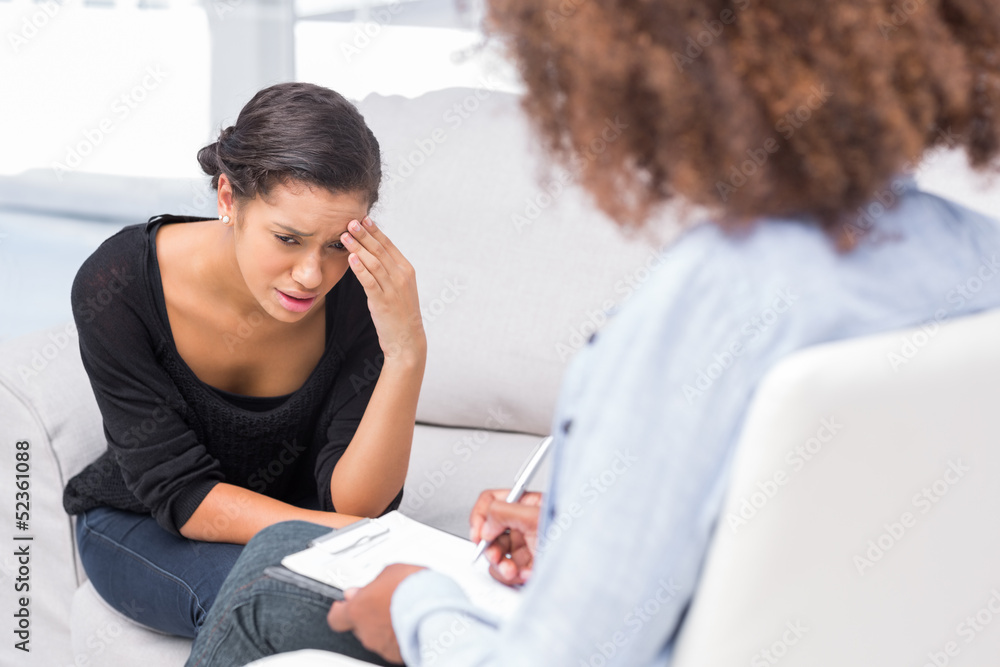 Woman crying on sofa while therapist is taking notes