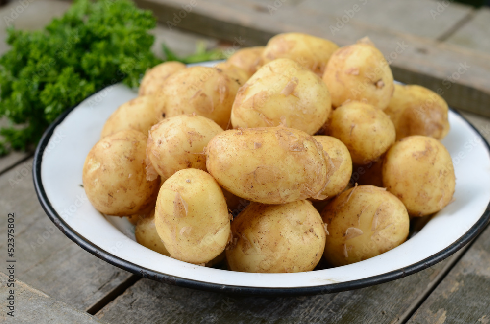 Young potato in metal bowl on wooden background Young potato in metal bowl on wooden background