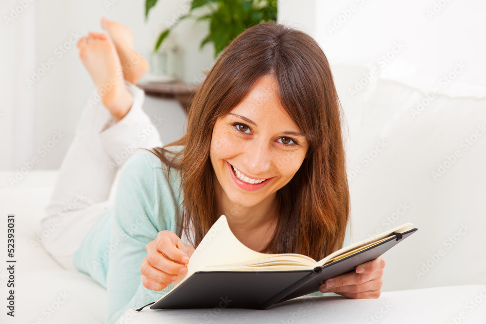 Young woman stretching comfortably on couch and reading a book Young woman stretching comfortably on couch and reading a book