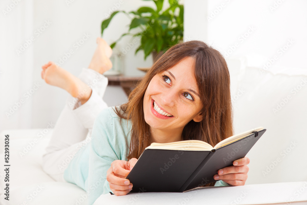 Young woman stretching comfortably on couch and reading a book Young woman stretching comfortably on couch and reading a book