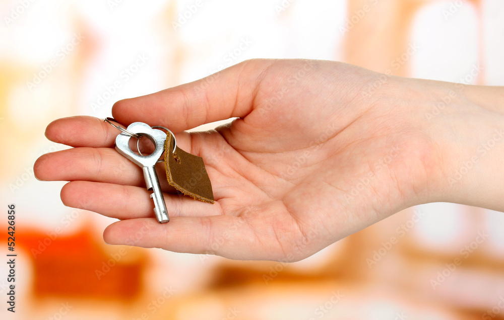 Key with leather trinket in hand on bright background