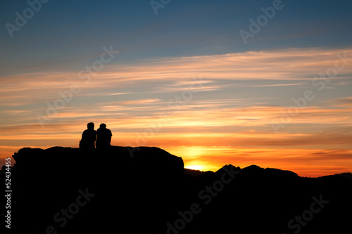 Couple having relax on top of a rock at sunset