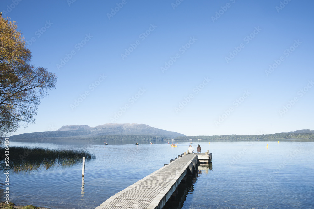Naklejka premium Jetty on Lake tarawera, with couple seated in distance.
