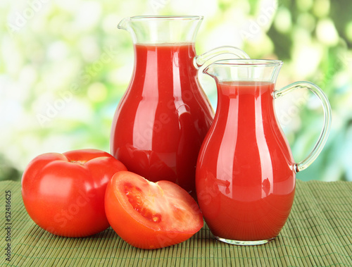 Tomato juice in pitchers on table on bright background