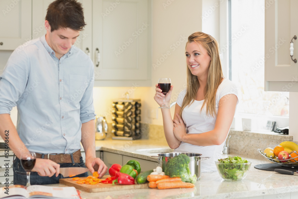 Man cutting vegetables with woman drinking wine