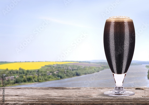 Frosty glass of dark beer  with summer scene background