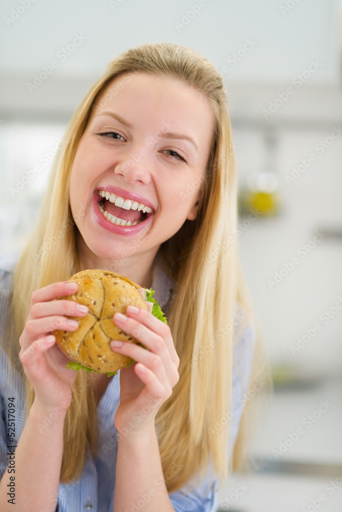 Smiling teenager girl eating sandwich in kitchen