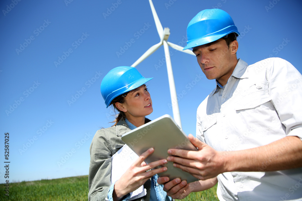 Engineers looking at wind turbine site with tablet Engineers looking at wind turbine site with tablet