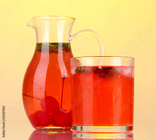 Cherry drink in pitcher and glass on yellow background.