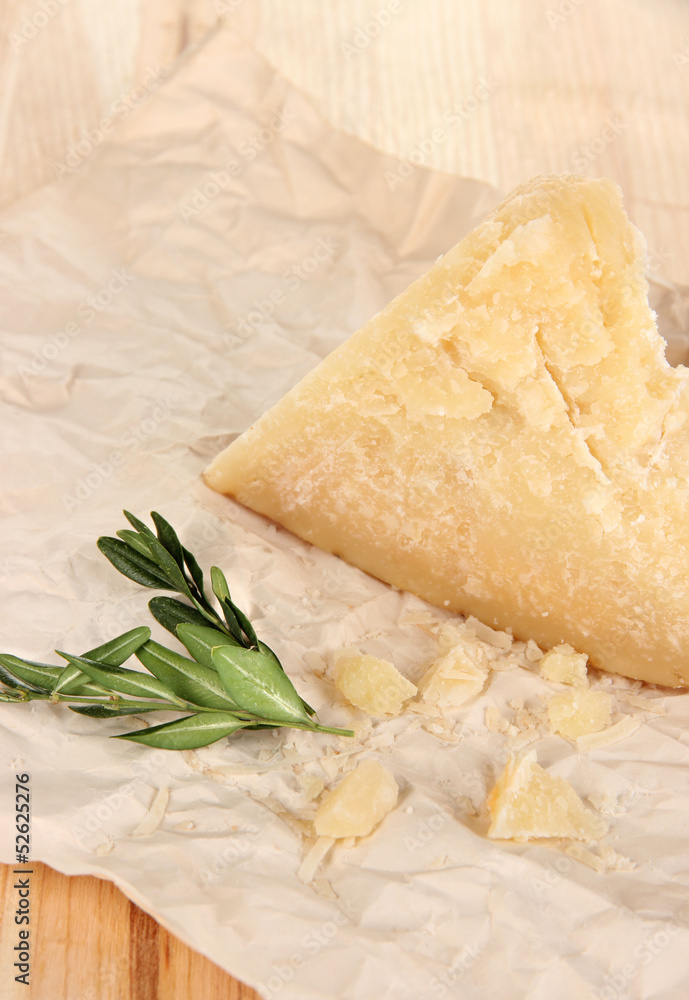 Piece of Parmesan cheese on paper on wooden table close-up Piece of Parmesan cheese on paper on wooden table close-up