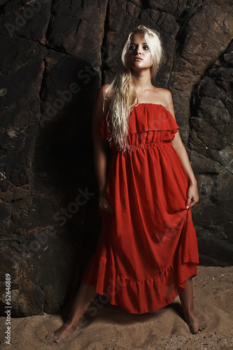 Beautiful blond woman in red dress near the rock
