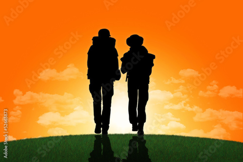 couple of backpackers walking on a top of a hill at sunset