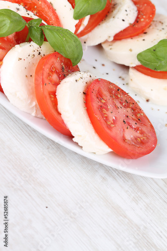 Tomato and mozzarella with basil leaves on a white plate