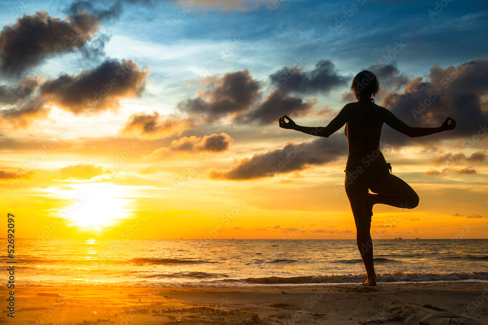 Girl practicing yoga by the sea at sunset.