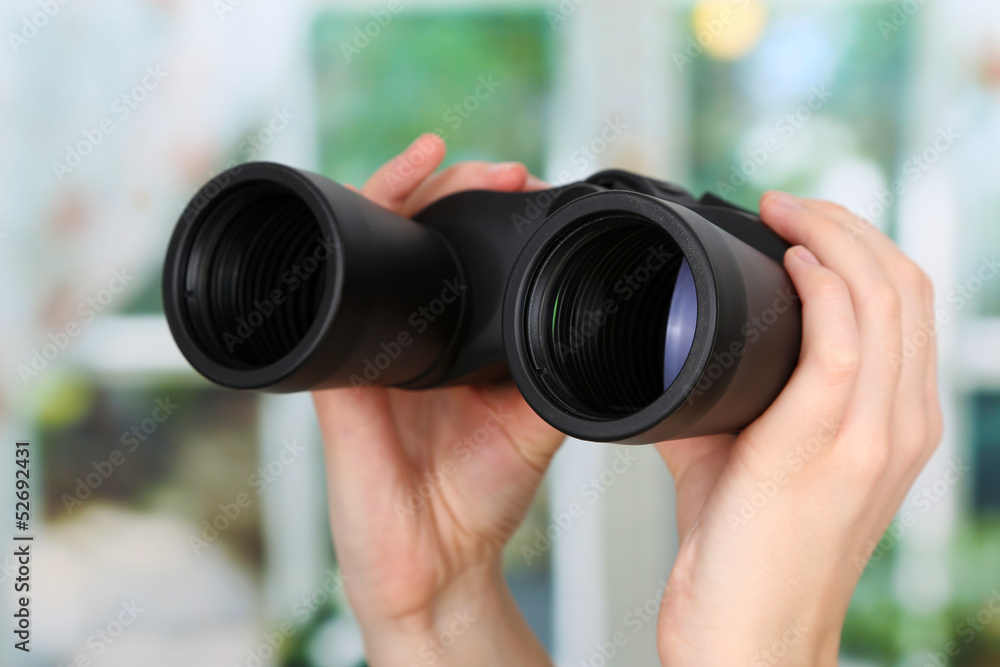Black modern binoculars in hands on window background