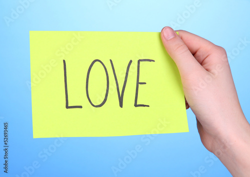 Love word on piece paper in hand on blue background