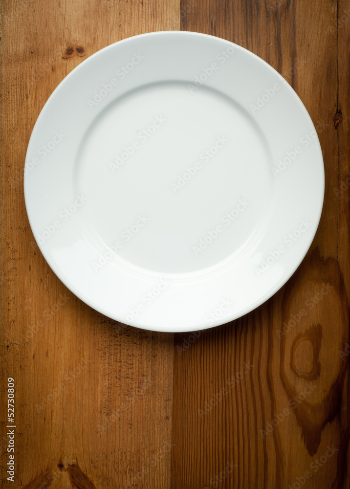 Empty white plate on wooden table Empty white plate on wooden table