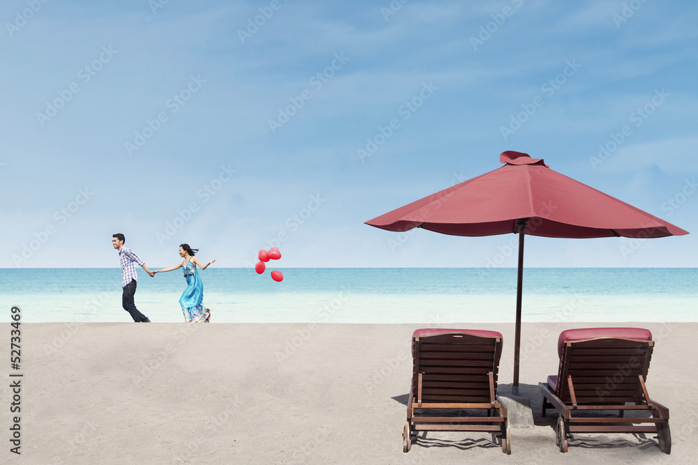 Obraz premium Beautiful couple run near beach chairs and umbrella