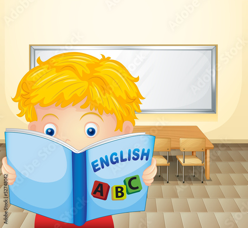 A boy reading a book inside the classroom