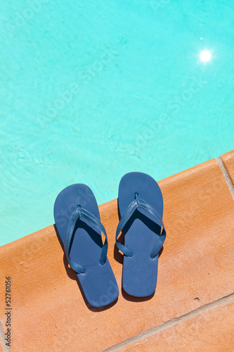 One pair of blue slippers on the edge of swimming pool.