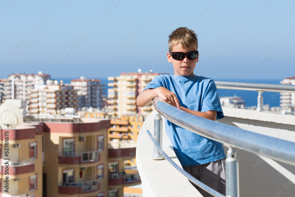 boy stands on balcony of hotel on background of cityscape