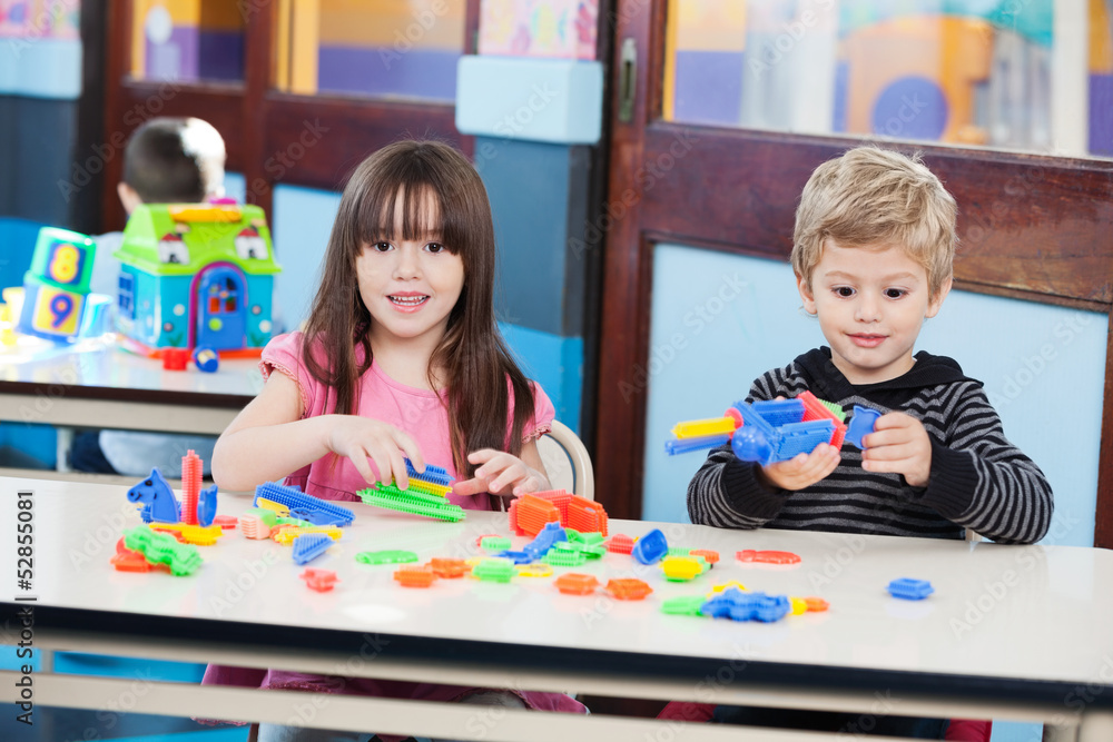 Fototapeta premium Cute Girl With Friend Playing Blocks At Desk In Classroom