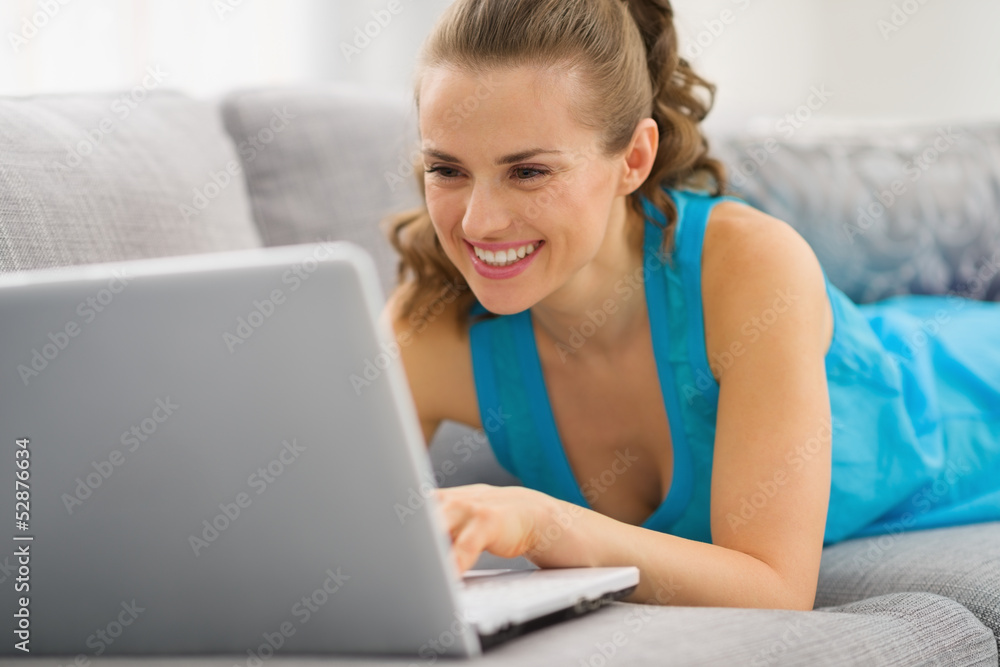 Smiling young woman laying on couch with laptop Smiling young woman laying on couch with laptop