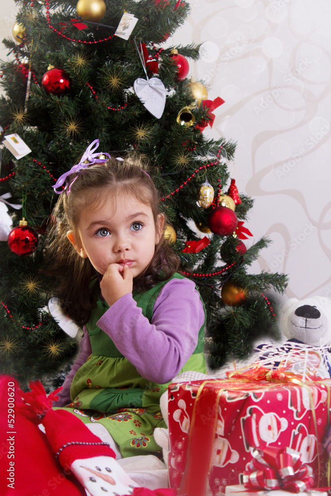 Little girl under Christmas tree with gifts