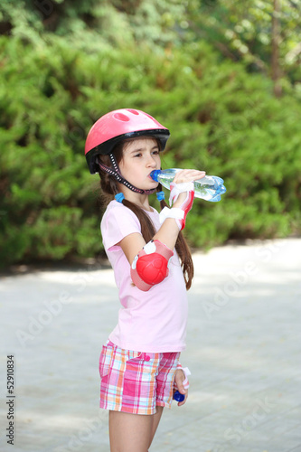 Little girl in roller skates drinking water at park