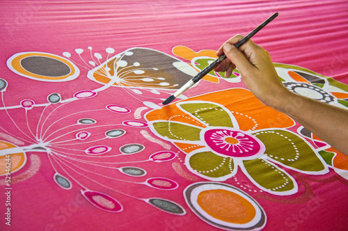 An artist paint the floral motif on a red silk batik fabric