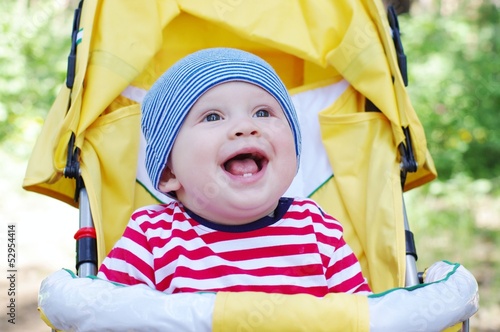 lovely smiling baby boy outdoors on yellow baby carriage