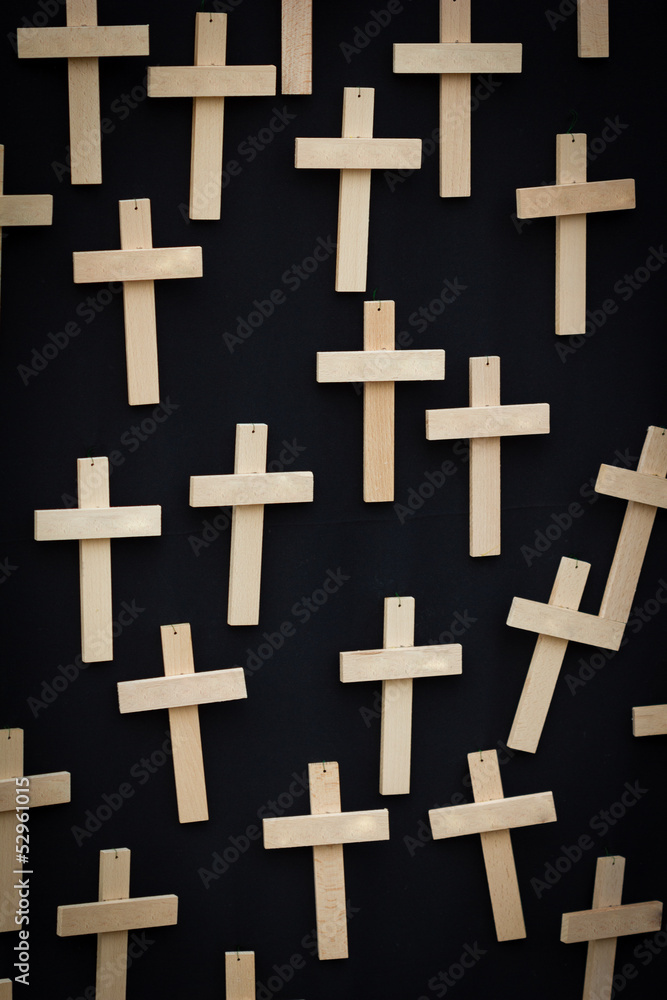 25 plain handmade wooden crosses suspended on a black canvas