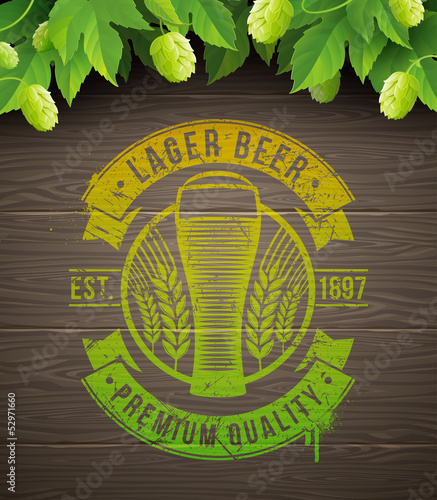 Beer emblem painted on wooden surface and ripe hops and leaves