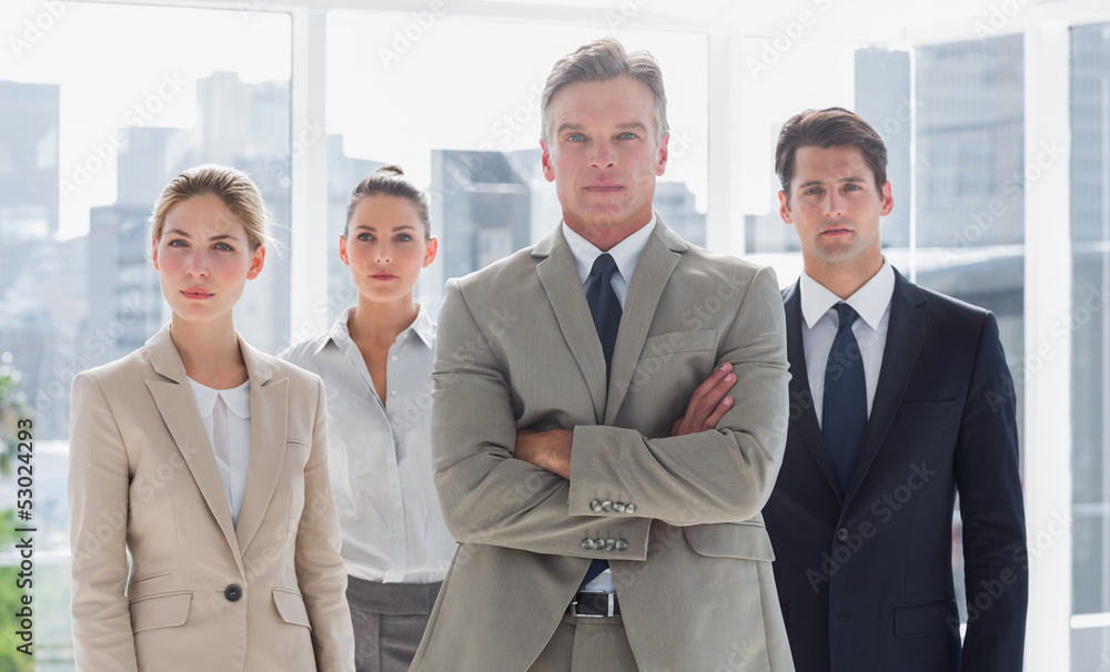 Boss with his arms folded standing with serious colleagues behin Boss with his arms folded standing with serious colleagues behin