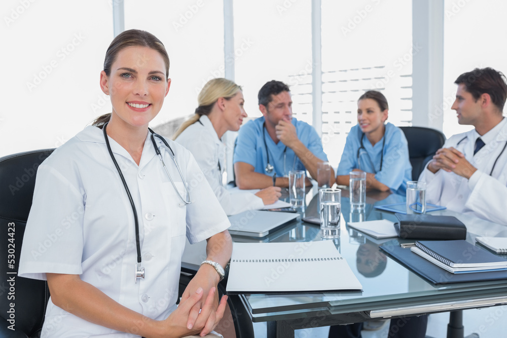 Smiling woman doctor looking at the camera in front of her team Smiling woman doctor looking at the camera in front of her team