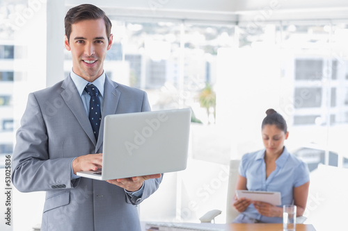 Businessman using laptop standing in office smiling at camera
