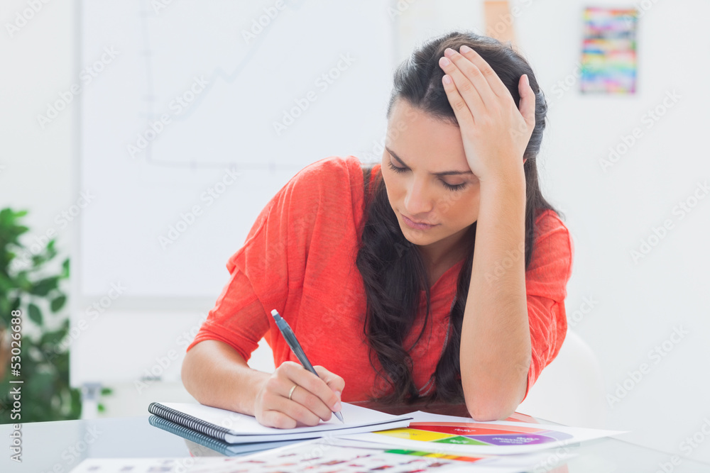 Tired designer holding her head while she is drawing Tired designer holding her head while she is drawing