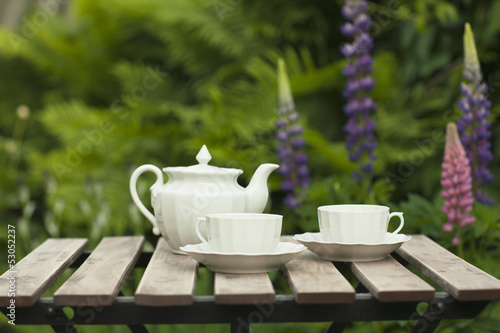 Белые чашки и чайник на столике в саду