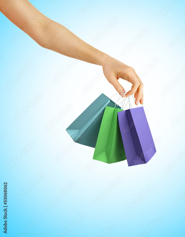 Hand with color shopping bags on blue background