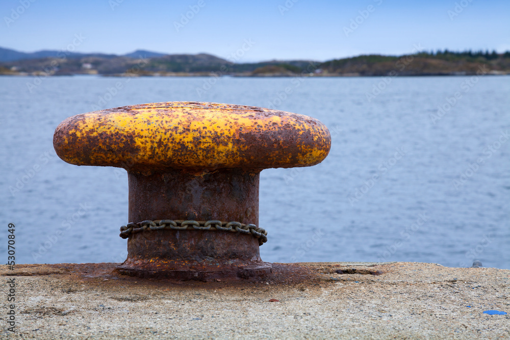 Old rusted yellow mooring bollard with chain on pier Old rusted yellow mooring bollard with chain on pier