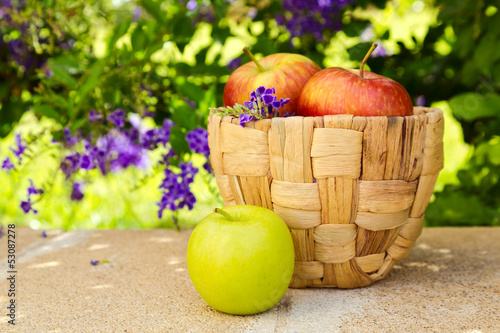 Basket with apples on stone surface over beautiful flower garden