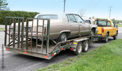 Fotografie Cadillac on a flatbed and towed by yellow truck