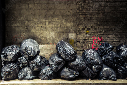 Obraz na plátne Black trash bags piled up against grungy urban wall