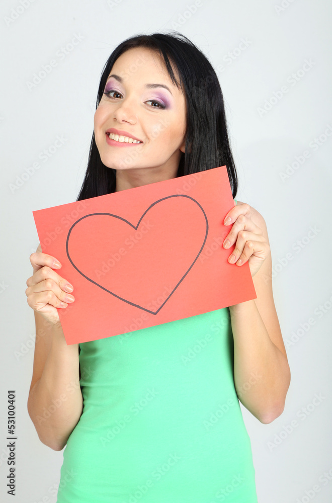 Young woman holding red painted heart on grey background Young woman holding red painted heart on grey background