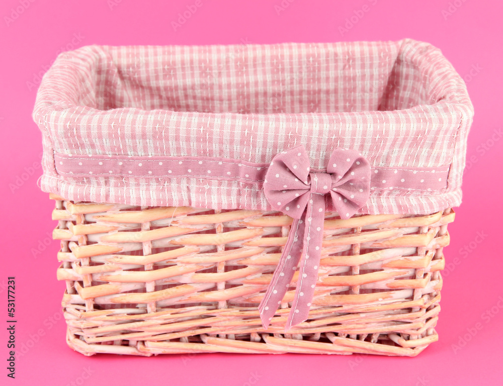Wicket basket with pink fabric and bow, on color background Wicket basket with pink fabric and bow, on color background