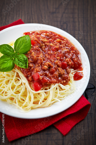 Spaghetti bolognese and green basil leaf on white plate